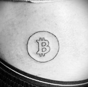 Черно-белое фото тату символа Bitcoin на пояснице. Минималистичный рисунок татуировки.