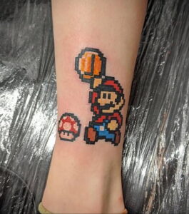 Фото тату с изображением Марио из игры Super Mario Bros. и красного гриба, выполненное в пиксельном стиле 8-bit. Яркий рисунок на ноге.
