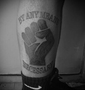 Фото тату сжатой руки в кулаке с надписью "By Any Means Necessary" ("Любыми средствами"). Черно-белый рисунок татуировки, эскиз тату в стиле гранж.