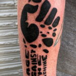 Фотография татуировки на руке в стиле Rage Against the Machine с изображением сжатого кулака и надписью "Rage Against the Machine". Черно-белый рисунок.