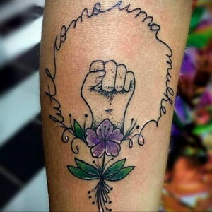 Фото тату на предплечье: кулак, сжимающий цветок, окруженный надписью и листьями. Цветная татуировка.