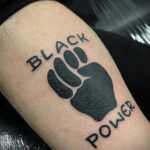 Фото тату на ноге: стилизованное изображение черной лапы с надписями 'BLACK' и 'POWER', символизирующее силу и гордость.