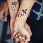 Фото парных тату: черные короны над буквами "P" на запястьях мужчины и женщины. Элегантный и минималистичный дизайн.