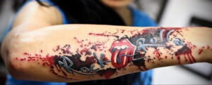 Фото тату с изображением языка и губ Rolling Stones и надписью 'Rock'n'Roll' на руке. Татуировка выполнена в стиле гранж и имеет яркий, бунтарский вид.