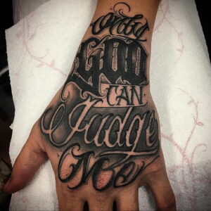 Фото тату надписи 'Only God Can Judge Me' на руке, выполненной в стиле blackwork с использованием каллиграфического шрифта. Подходит для тех, кто верит в высшую силу.