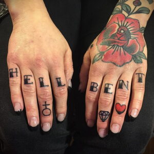 Фото тату: надписи 'HELL' и 'BENT' на пальцах, дополненные символами креста, бриллианта и сердца, выполненные в черном цвете.