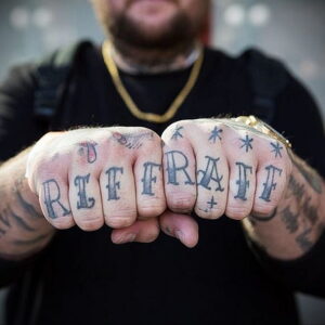 Фото тату: татуировка надписью 'RIFF RAFF' на костяшках пальцев, украшенная звездами. Дерзкий стиль, яркие цвета, мужская рука.