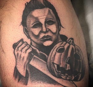 Фото тату Майкла Майерса с тыквой в стиле реализм. Черно-белая татуировка на руке.