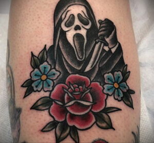 Татуировка Ghostface с красными и голубыми цветами. Маска злодея изображена на фоне ярких цветов, что создает контраст между красотой и ужасом.