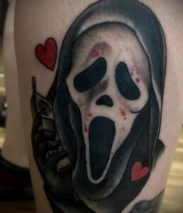 Яркая татуировка на руке с изображением Ghostface из фильма "Крик". Маска злодея выполнена в стиле old school с добавлением красных сердец.