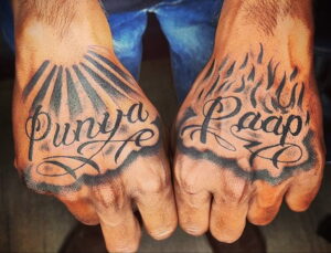 Фото тату на ладонях с надписями 'Punya' и 'Paap' на хинди, окруженными лучами света и пламенем.