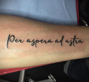 Фото тату: надпись "Per aspera ad astra" на руке. Черная надпись каллиграфическим шрифтом.
