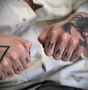 Фото тату: татуировки на пальцах, включая скорпиона и надписи 'FUCK' и 'MAN'. Черно-белые татуировки.