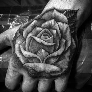 Фото тату: татуировка розы в стиле blackwork на руке, выполненная полностью черным цветом с использованием геометрических узоров и теней.