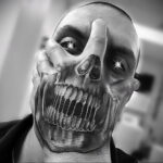Фото тату: реалистичная татуировка черепа, занимающая большую часть лица, с яркими, искрящимися глазами, выполненная в черно-белых тонах.