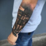 Фото тату на руке с изображением маяка, окруженного волнами. Реалистичный стиль и детализированная проработка.