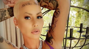 Фотография Amber Rose с татуировкой на лбу 'Killa Kill' и большим рисунком розы с бабочкой на руке. Она позирует в стильных очках.