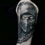 Фото черно-белой татуировки Скорпиона из Mortal Kombat на руке. Детализированное изображение лица и маски персонажа с использованием теней и контуров.