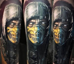 Фото реалистичной татуировки Скорпиона из Mortal Kombat на руке. Детализированное изображение лица и маски персонажа с яркими цветами и тенями.