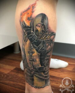 Фото тату Скорпиона из Mortal Kombat на ноге. Детализированный рисунок с изображением персонажа, выпускающего огненный шар.