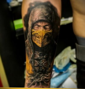 Фото тату на предплечье с изображением Скорпиона из Mortal Kombat. Детализированный рисунок с желтой маской и темной одеждой.