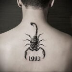 Фото тату черного скорпиона с датой '1993' на шее мужчины. Лаконичный рисунок с четкими контурами и символическим значением.