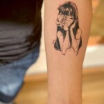Черно-белое фото тату на предплечье с изображением девушки с расколотым лицом, сочетающим красоту и ужас.