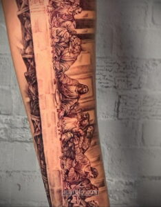 Фото тату реалистичного изображения сцен из Страстей Христовых на руке, выполненное в черно-серых тонах с добавлением текстур и надписей.