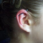 Фото пирсинга индустриального хряща уха с двумя серебряными шариками. Ухо девушки выглядит стильно и современно.