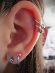 Фото тату: прокол уха с несколькими серебряными кольцами и гвоздиками. Детализированный вид украшений на ухе.