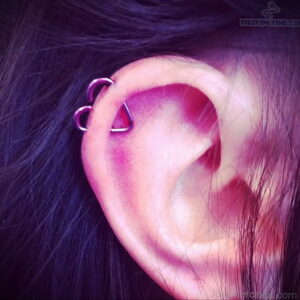 Фото тату: пирсинг уха с двумя фиолетовыми кольцами в хряще. Крупный план, темные волосы, яркий цвет.