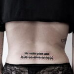 Фото тату на спине девушки: надпись "fake russian prison tattoo", имитация татуировки заключенного, минималистичный стиль, черно-белый рисунок.