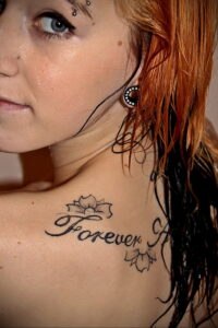 Фото тату с надписью "Forever" на ключице женщины. Элегантный шрифт и цветочные элементы.