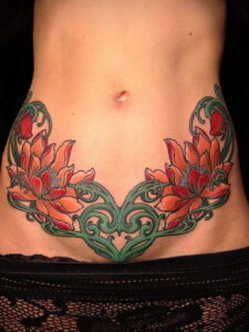 Фото тату: Цветная татуировка с изображением больших красных цветов и зеленых листьев, расположенная на животе женщины.