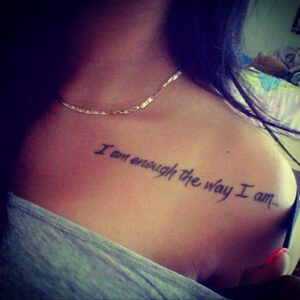 Татуировка с надписью 'I am enough the way I am...' на женской ключице. Простой, но вдохновляющий рисунок татуировки, выполненный черными чернилами.
