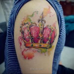 Фото тату на плече: акварельная корона в нежных розовых и золотых тонах. Красивый рисунок татуировки, выполненный в технике акварели.