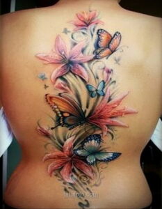 Фото тату с изображением лилий и бабочек на спине. Рисунок выполнен в реалистичном стиле с использованием ярких и нежных цветов.