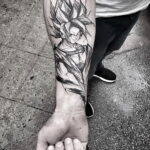 Фото тату персонажа Гоку из аниме Dragon Ball Z на предплечье мужчины. Черно-белая графика, динамичная поза и детализированная прорисовка.