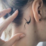 Фото тату: маленькая черная татуировка птички, выполненная за ухом девушки, выглядит изящно и минималистично.