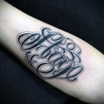 Фото татуировки на руке с надписью "Olaya O" в стиле Cholo. Детализированный рисунок с витиеватыми линиями и узорами.