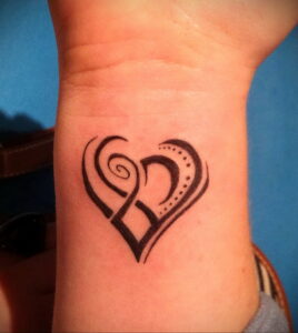 Фото тату на запястье в виде сердца, выполненного в стиле трайбл. Черный рисунок татуировки дополнен точками и завитушками, придающими ему изящество и оригинальность.
