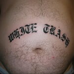 Фото татуировки надписи 'White Trash' на животе. Черный контурный рисунок, выполненный готическим шрифтом. Эскиз татуировки с провокационным смыслом.