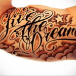 Фото тату на руке: надпись "Give the Dream" в каллиграфическом стиле, окруженная звездами и облаками. Черно-коричневая гамма.