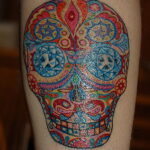 Фото тату черепа в стиле Sugar Skull на икре. Многоцветный рисунок с детальной прорисовкой узоров и орнаментов. Отличный эскиз тату для ценителей мексиканской культуры.