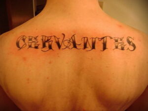 Фото тату на спине с надписью "Cervantes" в готическом стиле. Черно-белый рисунок, декоративные шрифты, классический дизайн.