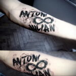 Фото тату с именами 'Anton' и 'Julian' и символом бесконечности на руке. Минималистичный дизайн в черном цвете с эффектом акварели.