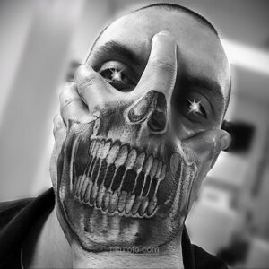 Фото тату на лице: реалистичный череп, эффект оптической иллюзии, черные и серые тона, провокационный дизайн.