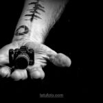 Черно-белое фото руки, держащей миниатюрную камеру Fujifilm. На предплечье видны татуировки в виде геометрических фигур и абстрактных узоров. Символизирует любовь к фотографии.