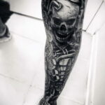 Фото тату: детализированный черно-белый череп с змеями, обвивающими ногу. Реалистичный рисунок татуировки с высокой детализацией.
