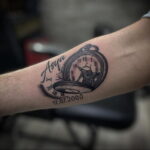 Фото татуировки: карманные часы с именем "Asya" и датой "17.07.2000", выполненные в черно-серых тонах на руке.
